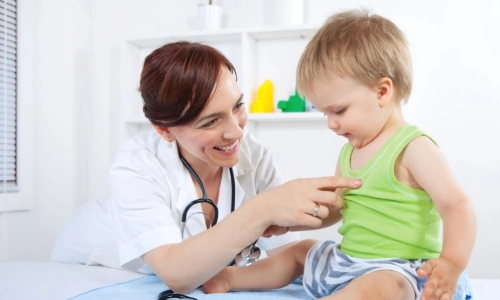A doctor pointing at a toddlers chest where she will place a stethoscope to listen to its lungs