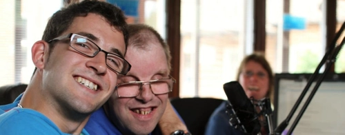 Two people hugging. There is a girl smiling in the background