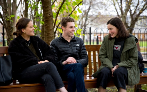 Three students sit on a bench