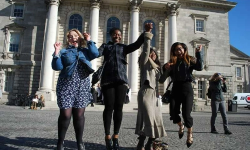 Four students jumping up for a picture on the Front Square of Trinity College Dublin