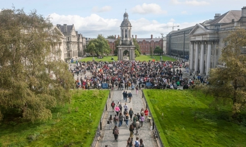 Image taken from an upstairs room, looking down on Trinity's Front Square during Freshers' Fair 2023. Front Square is crowded with people.