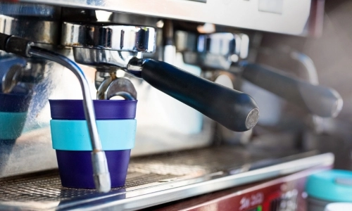 Image of a blue reusable coffee cup being filled at a barista coffee station.