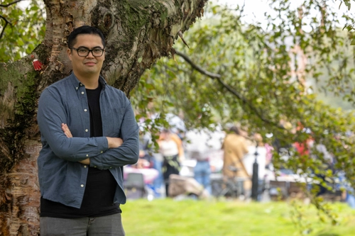 Photo of Nathan Cruz standing in front of a tree. He has his arms folder and is looking at the camera.