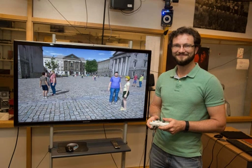 A degree student standing beside a TV screen showing a CGI presentation