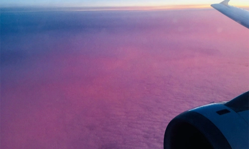 A photo taken from an airplane video where you can see a purple sky and the wing of a plane