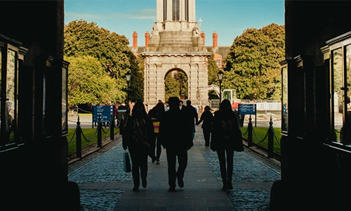3 students walking in through the front arch of Trinity College Dublin