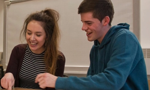 2 students laughing and looking at study material