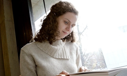 A picture of a student sitting by window reading a book