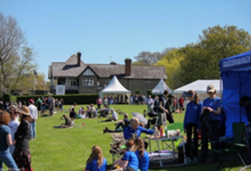 Groups of people sitting on the lawn in front of Trinity Boat house in the War Memorial Park