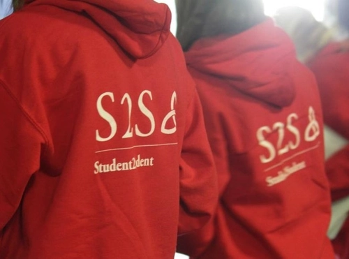 Two students wearing red hoodies with their back to the camera. The hoodies say Mentor on the back.