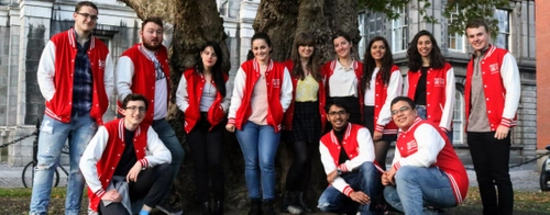 Student 2 Student Society in red and white varsity jackets standing in a line looking at the camera and smiling.