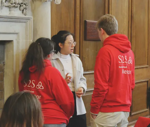 Two S2S Mentors with their backs to the camera talking to a student wearing a white jacket and top at the S2S Award Ceremony