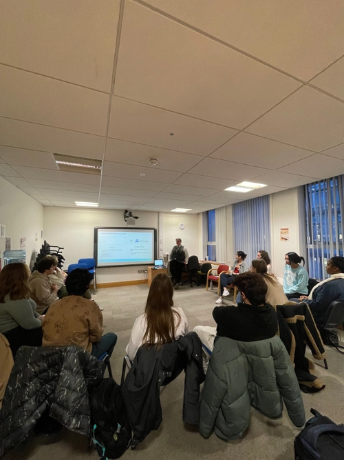 photo of a room of students sitting in a circle, looking at a board