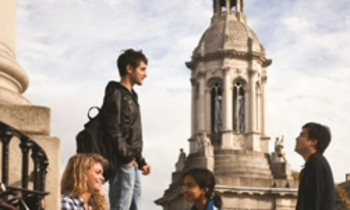 Four students talking in the Front Square of Trinity College Dublin in front of the Campanile (bell tower)