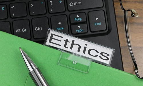 Image of the word ethics printed on a label attached to a green folder, on top of a keyboard.