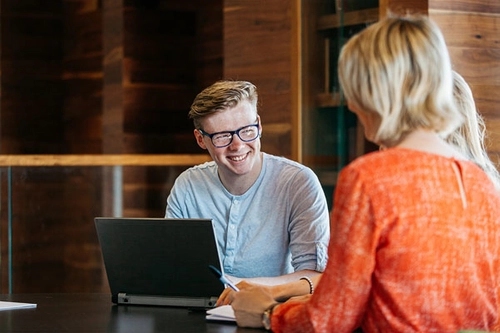 Two students in conversation with a laptop