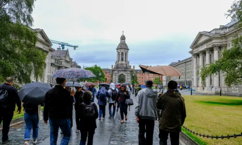 People holding unbrellas walking in to the Front Square of Trinity College Dublin