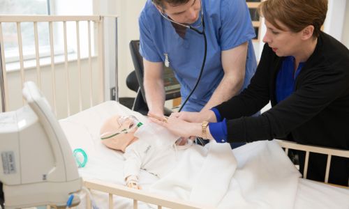 A consultant explaining to a doctor how to do CPR on dummy baby