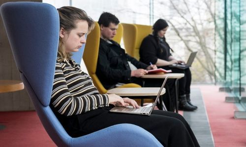 Three people seated separately working on their laptops in the library.