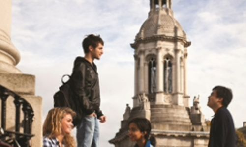 Four students talking in the Front Square of Trinity College Dublin in front of the Campanile (bell tower)