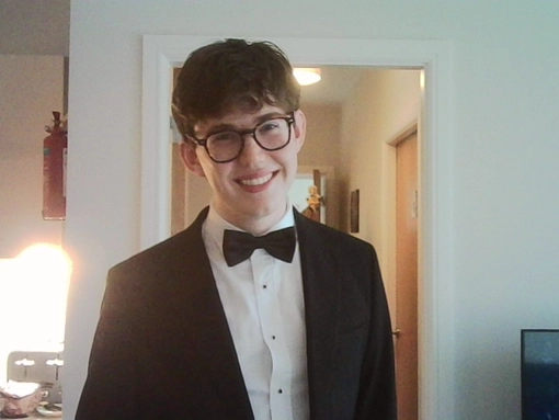 Student wearing a tux with short dark hair wearing glasses