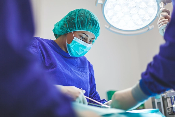 A surgeon wearing a mask, hair cap and gloves operating on something