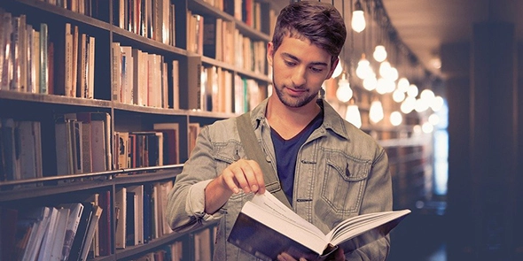 A young person in a library opening a book
