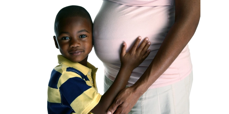 Small child placing his ear on his pregnant mothers belly.