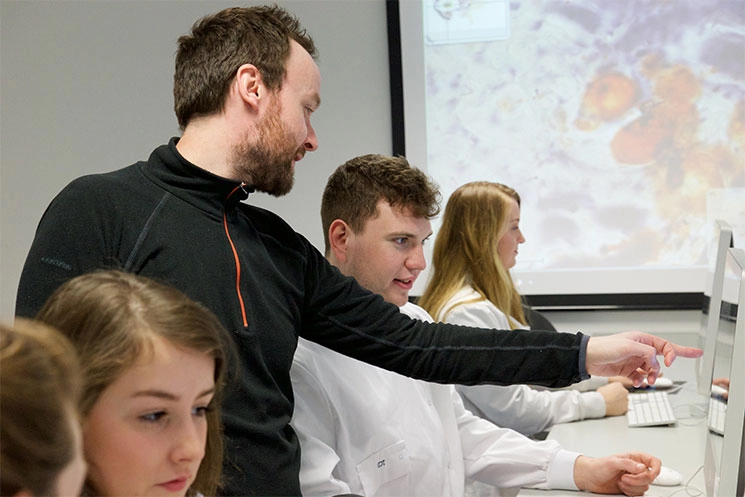 A teacher pointing at something on a screen to a student