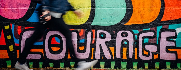 Man walking past graffiti wall spelling courage