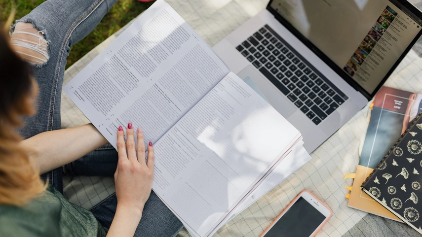 A student sitting on grass with text book and laptop open