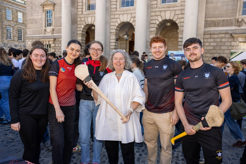 Linda standing with members of the Trinity LGFA and GAA teams. Linda and one other student are holding hurley sticks.