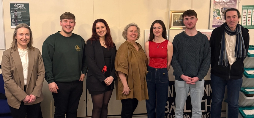 Celebrations to launch Éigse na Tríonóide in Seomra na Gaeilge. Linda is standing for a photo with staff and students, all are smiling for the camera. There are two staff members, and four students in the photo.