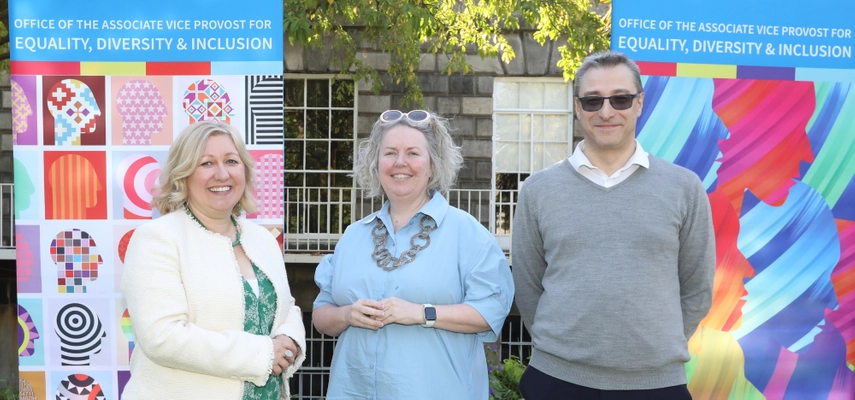 Linda with Lorraine Leeson and Graeme Watson, smiling for a photo in the Provost's Garden in front of colourful pull up banners.