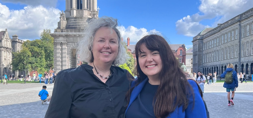 Linda and Lianne Quigley smiling for a photo on Trinity Front Square with blue skies and Campanile in the background.