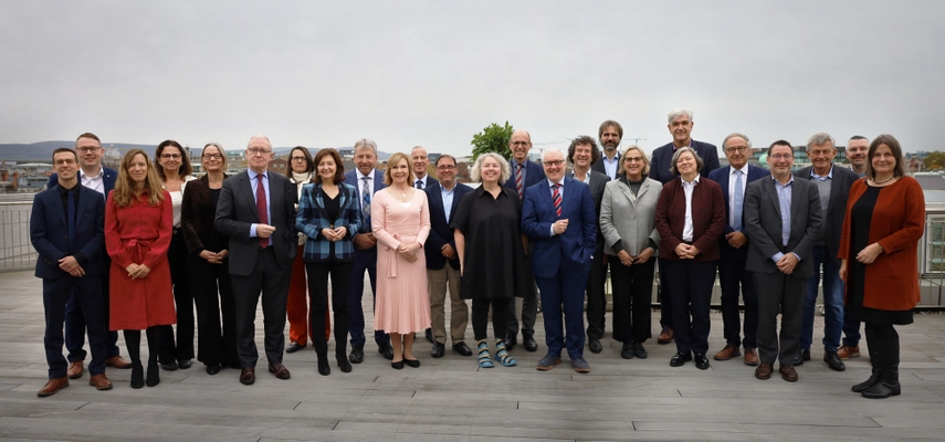 Large group photo taken on a balcony. All smiling at the camera. Cloudy sky in the background.