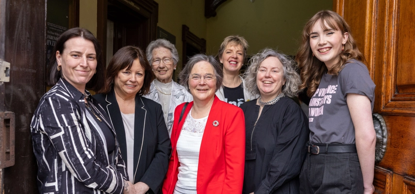Group of seven women standing for a group photo in a doorway. All smiling at the camera.