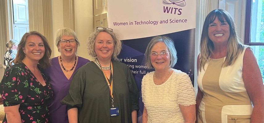 Five women smiling for a photo, standing in front of a pull-up banner.