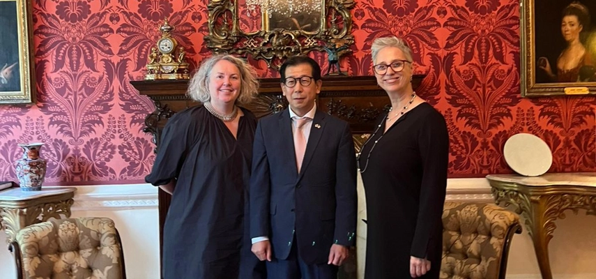 Linda Doyle standing alongside Ambassador Yong-kil Kim and Emma Stokes. Mantelpiece in background surrounded by red wallpaper and mirror.