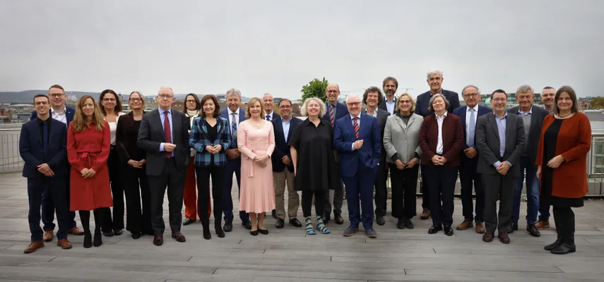 Large group photo taken on a balcony. All smiling at the camera. Cloudy sky in the background.