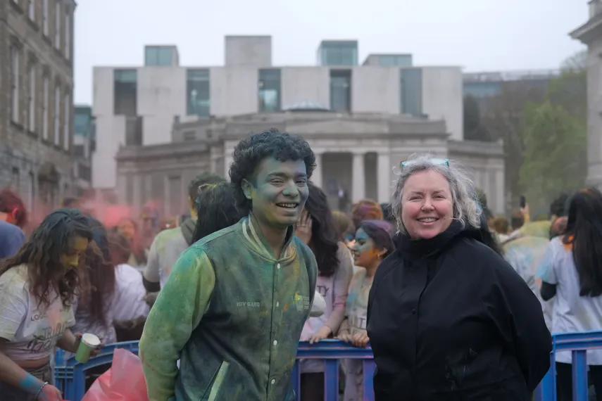 Linda standing in front of the Holi celebration on Front Square with President of Trinity Indian Society, Yuv Garg. Yuv is covered in colourful Gulal from the Holi celebration.