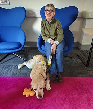 Image of Dr Patricia McCarthy seated with her guide dog Gaston on the floor beside her.