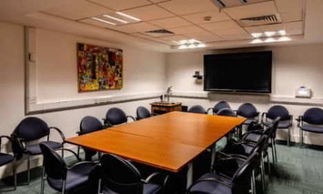 Room b1.04 in TBSI. The room has a large conference table and chairs with a large screen and painting on the walls