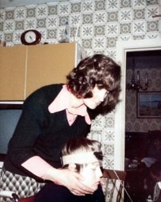 Christy Nolan wearing his unicorn stick with his mother Elizabeth Nolan standing above him. The unicorn stick was a tool that Christy used to type with.