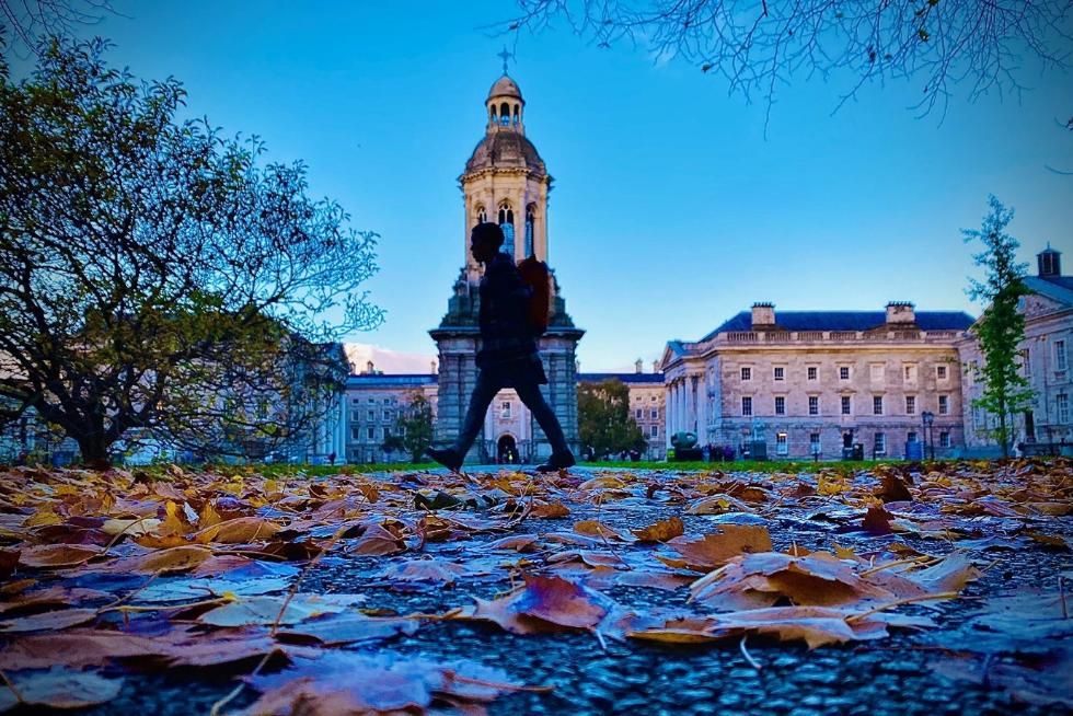 A view of the campanile at TCD with a person walking in silhouette and leaves in the foreground