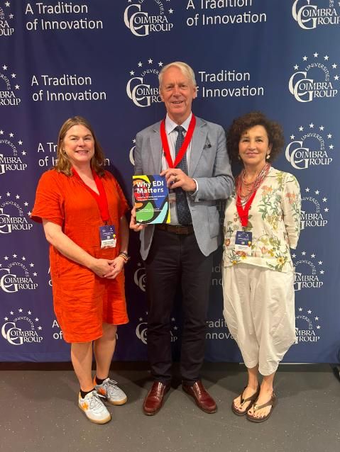 Three people standing together with centre person holding a book