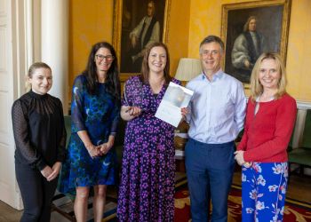 Five people standing in a line beside a person holding an award