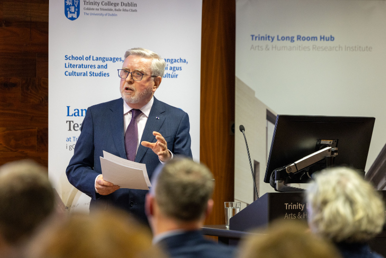 Pat Cox standing in front of a podium addressing a seated audience, during the Languages 250 at Trinity Opening Ceremony.