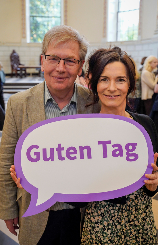 Jürgen Barkhoff and Mary Cosgrove holding a 'Guten Tag' sign.