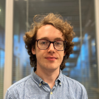 Headshot of Pearce Clancy wearing glasses and a light blue shirt in front of a glass office wall.